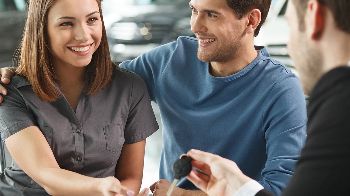 people cheerfully interact in a brightly lit car showroom, during a key exchange img