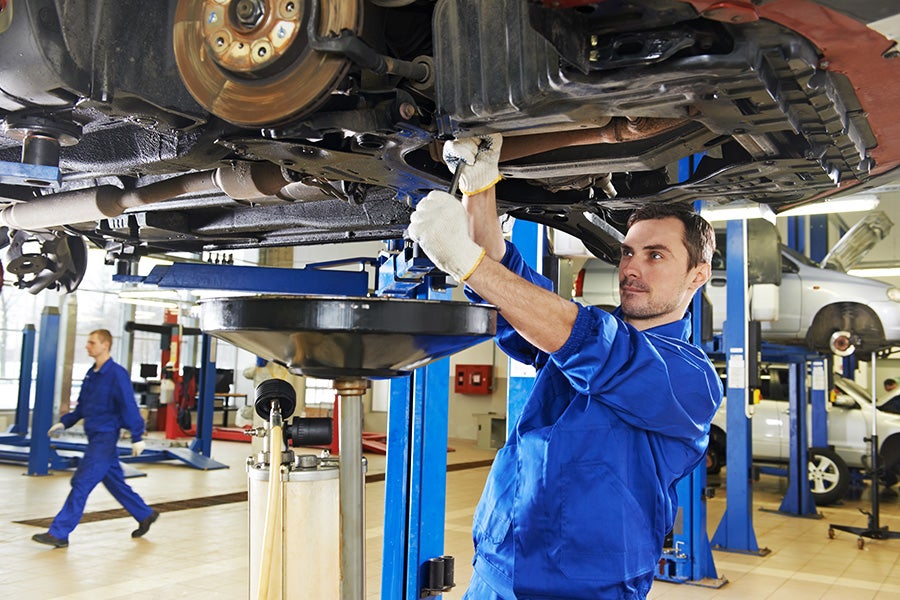 a caucasian mechanic in a blue uniform works intently on a car's undercarriage in a well-lit auto shop img
